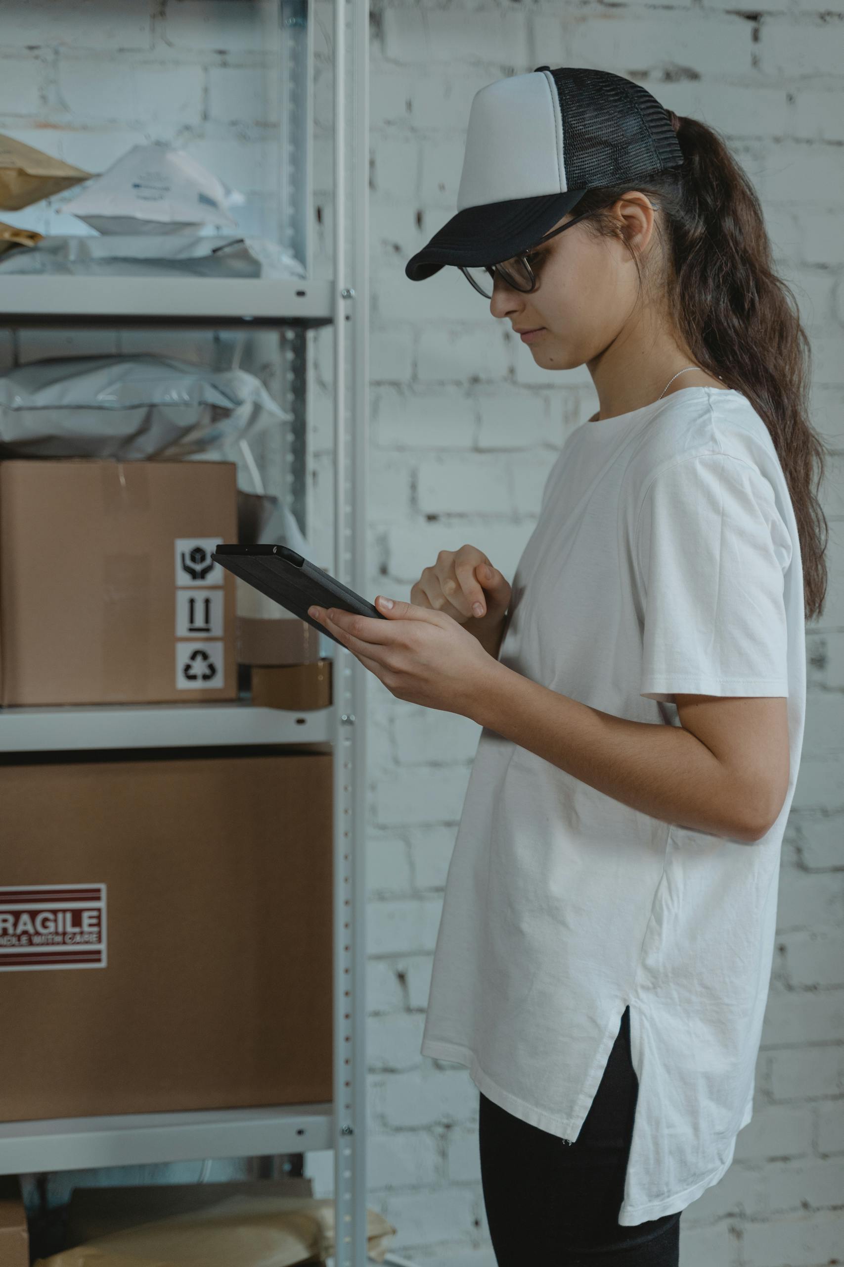 A woman in casual wear using a tablet for inventory management in a warehouse.